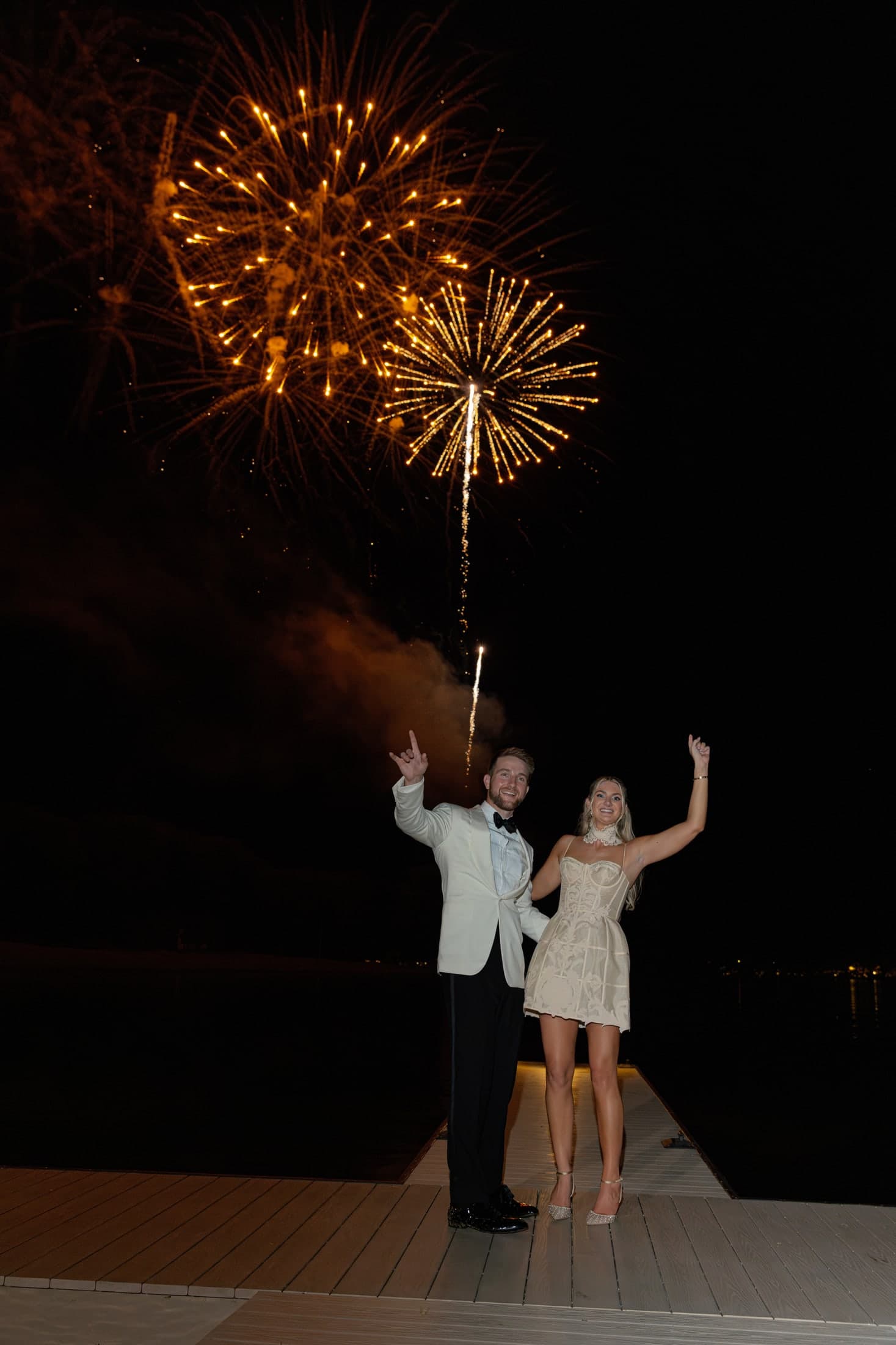 the couple cheering under gold fireworks on the dock